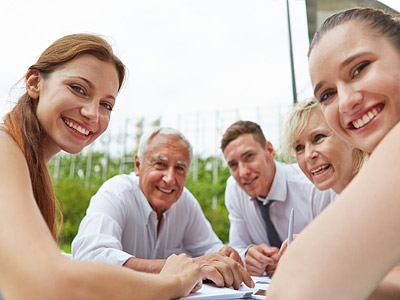 Eine Gruppe von fünf Personen lächelt in die Kamera, während sie um einen Tisch sitzen.