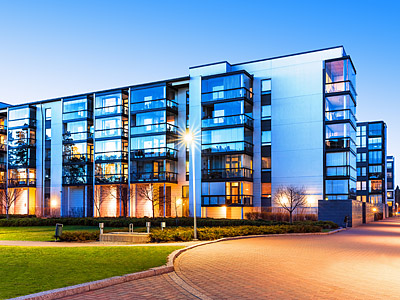 Moderne Wohnanlage mit Glasfassaden und begrüntem Außenbereich bei Dämmerung.